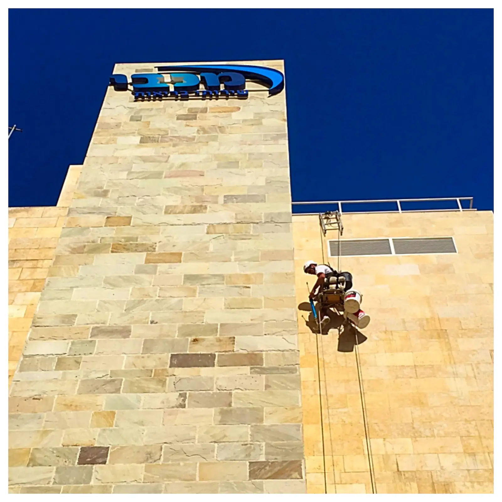 עובד הרמטיקו בסנפלינג מבצע איטום על חזית בניין מחופה אריחים לבנים